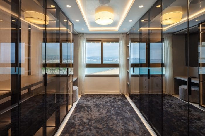 Walk-in wardrobe in smoked glass increasing the feeling of space. At the end of the wardrobe there is a vanity unit and stool right by the window with views across the bay.