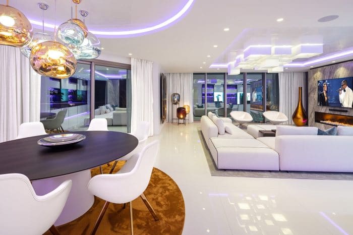Tom Dixon Melt lights hang gracefully over the custom-made dining table accompanied by Tom Dixon white leather chairs, contrasting with the circular burnt orange rug.